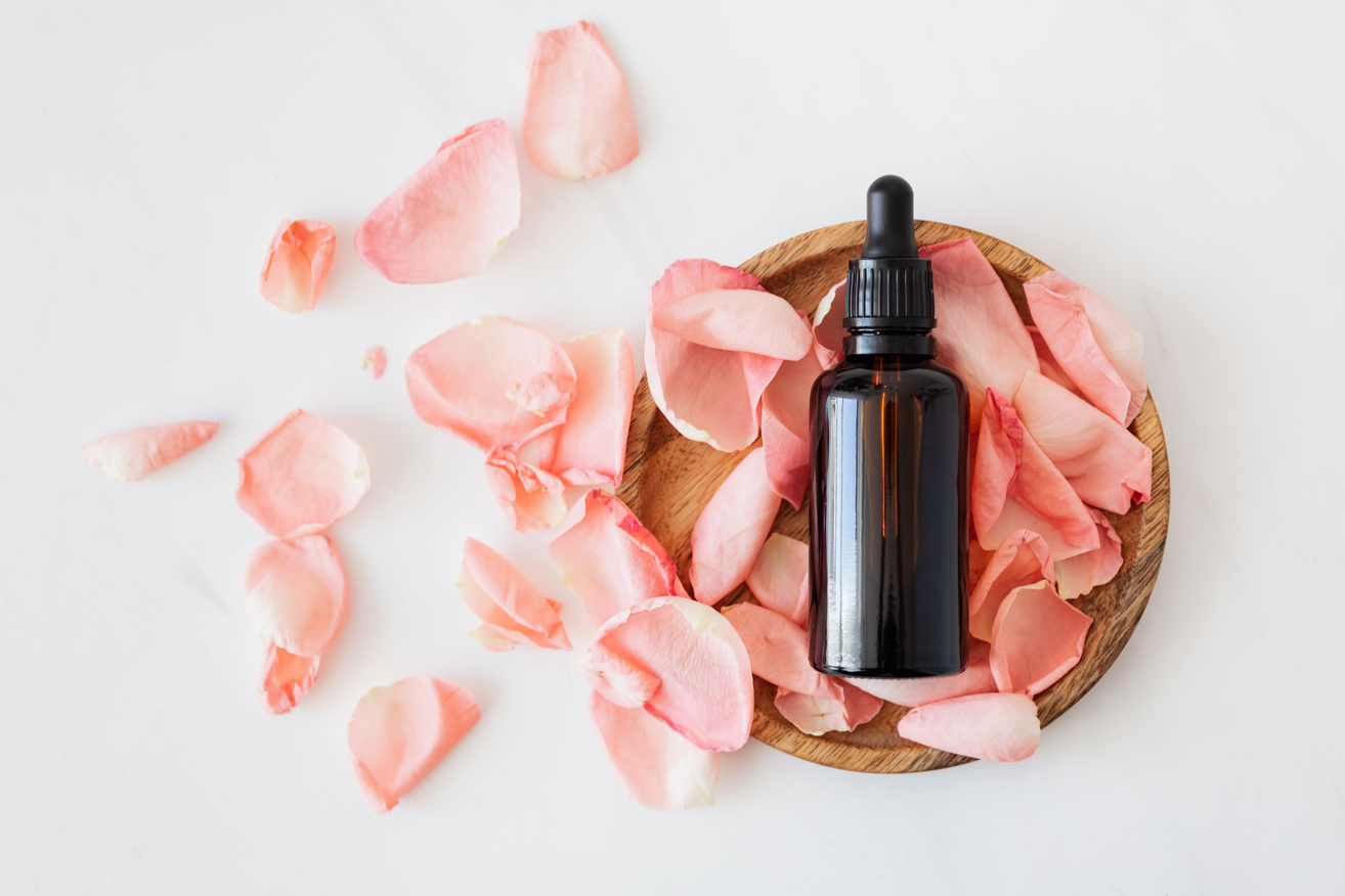 Composition of cosmetic bottle with pink rose petals and wooden plate